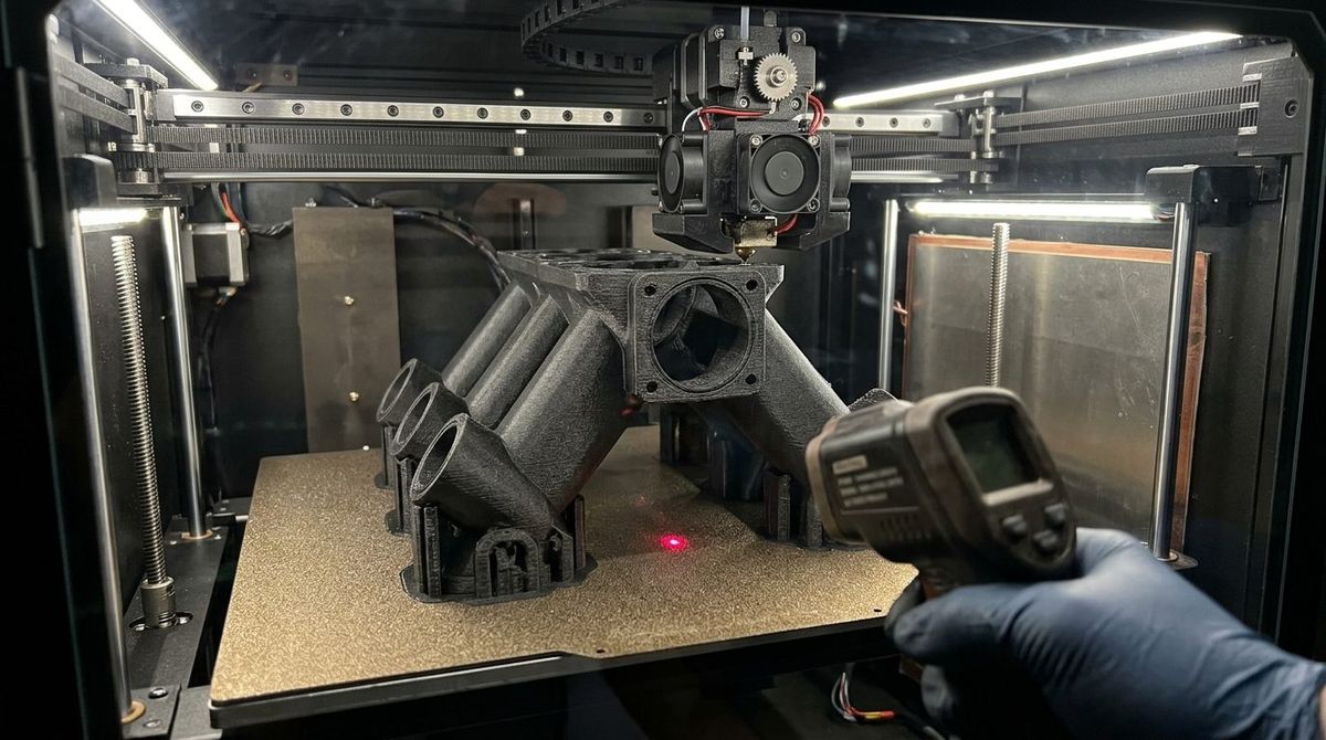 Close-up inside an enclosed 3D printer chamber showing a large carbon-fiber nylon gear print on a heated textured PEI build plate